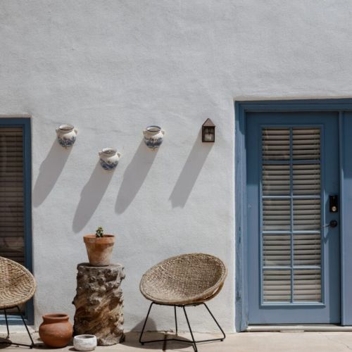 A peaceful patio setup with woven chairs, terracotta pots, and a classic stucco wall.