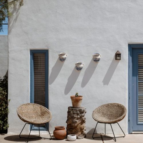 A peaceful patio setup with woven chairs, terracotta pots, and a classic stucco wall.